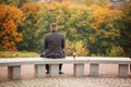 Lone man sitting on the stone bench and looking at nature. Back view. Autumn theme. Royalty Free Stock Photo