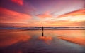 A lone man standing on a beach at sunset