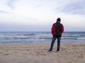 A lone man is standing on an empty sea beach and looking into the distance on a cold overcast autumn day