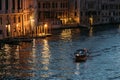 Lone motorboat floats the Grand Canal in Venice in glowing lights against the backdrop of blue water on a summer evening