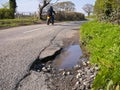 A lone motorcyclist passes unrepaired surface damage to tarmac on a rural road Royalty Free Stock Photo