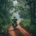 A lone motorcyclist rides along a muddy, winding road through a dense, mist-shrouded jungle, evoking a sense of adventure