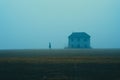 a lone person standing in front of a house in the fog