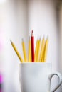 A lone red pencil in front of a group of yellow pencils in a white cup