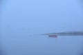 A lone red rowboat or skiff in heavy fog