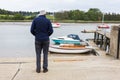 A lone retired male standing on the edge of a quay and looking out over the river and the boats that are moored up close by