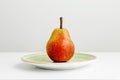 A lone ripe pear on a green plate on a plain white surface and a white background too