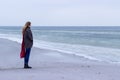 Lone sad beautiful girl walking along the shore of the frozen sea on a cold day, rubella, chicken with a red scarf on the neck Royalty Free Stock Photo