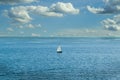 A lone sailboat out in the ocean with a nice breeze and a cloudy but clear sky.