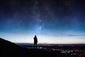 A Lone Silhouetted Hooded Figure. Standing On A Hill Looking Down On City Lights At Night With A Galaxy And Stars Rising In The Ni