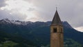 Lone standing steeple in reservoir Reschensee, South Tyrol, Italy, with snow-capped mountains and cloudy sky.