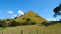 Lone steep grassy hill towers towards the sunny sky near scenic countryside road Royalty Free Stock Photo