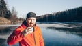 A lone tramp traveler stands on ice and drinks tea from a thermos