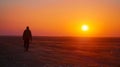 A lone traveler strays from the rest walking towards the distant horizon as the sun sets behind them. .