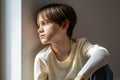 Sad boy orphan child sitting on windowsill at home, kid feeling lonely Royalty Free Stock Photo