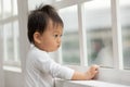 Lonely Adorable asian baby toddler standing in front of windows and looking outside waiting mom or dad come back home.Sad Baby