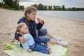 Lonely adorable eight years girl playing with doll on the autumn beach, mother and daughter game