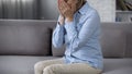 Lonely aging lady on sofa covering face, overwhelming problems, bad news Royalty Free Stock Photo