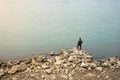 Lonely Asian fisherman standing on rocks in front of water
