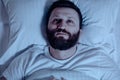 A lonely bearded man in bed at night cannot sleep, is unhappy and very tired. Sleep problems, stress, insomnia, bedroom, pajamas, Royalty Free Stock Photo