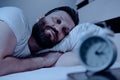 A lonely bearded man in bed at night suffers from insomnia and he watches the time on the alarm clock. Can not fall asleep, a Royalty Free Stock Photo