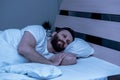 A lonely bearded man lies in bed at night and looks nowhere. Insomnia, pajamas, white bedding Royalty Free Stock Photo