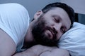 A lonely bearded man sleeps at night in bed with his arms folded under his head. Healthy sleep, pajamas, white bedding Royalty Free Stock Photo