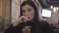 A lonely beautiful girl sits in a cafe and drinks a cocktail.