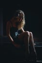 Sad beautiful girl sitting on black piano in the dark room Royalty Free Stock Photo