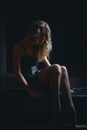 Sad beautiful girl sitting on black piano in the dark room