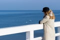 Lonely beautiful sad girl is standing on the pier on a sunny warm autumn evening at the sea Royalty Free Stock Photo