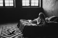 Lonely beautiful woman in the bedroom with large windows on the bed with a glass of wine relaxes. Black and white art photo in a Royalty Free Stock Photo