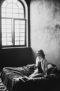 Lonely beautiful woman in the bedroom with large windows on the bed with a glass of wine relaxes. Black and white art photo in a Royalty Free Stock Photo