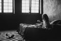 Lonely beautiful woman in the bedroom with large windows on the bed with a glass of wine relaxes. Black and white art photo in a Royalty Free Stock Photo