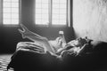 Lonely beautiful woman in the bedroom with large windows on the bed with a glass of wine relaxes. Black and white art photo in a Royalty Free Stock Photo