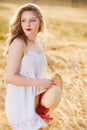 Lonely beautiful young blonde girl in white dress with straw hat