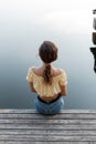 lonely beautiful young girl in fashionable clothes with jeans and a yellow top blouse sits on a wooden pier near the lake Royalty Free Stock Photo