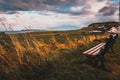 Lonely bench in a cold and windy coastal city, pointing to the sea with dramatic cloudy sky while grass is blown by the wind.