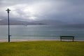 Lonely bench on the shore of the Atlantic Ocean, next to the lantern and a beautiful green lawn, Spain, mountain view, cloudy day Royalty Free Stock Photo