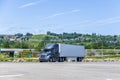 Lonely big rig dark semi truck with semi trailer stands in spacious parking lot Royalty Free Stock Photo