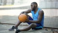 Lonely black basketball player sitting on stadium ground and holding ball, sport Royalty Free Stock Photo