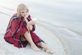 Lonely blond woman on the beach with cup of hot drink, warm red plaid Royalty Free Stock Photo