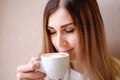 Lonely blonde girl sitting on a windowsill with a white cup with coffee with a heart, romantic mood. Royalty Free Stock Photo