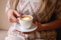 lonely blonde girl sitting on a windowsill with a white cup with coffee with a heart, romantic mood.