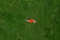 Lonely blonde woman in red dress lying on green grass closing her face with hand