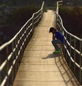 Lonely boy sitting on a suspension bridge Royalty Free Stock Photo