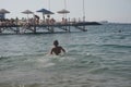 A lonely boy stands waist-deep in the sea, view from behind.