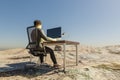 lonely businessman at pc work place in large desert environment remote work and digital nomad and climate crisis concept 3D