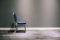 A lonely chair with silver legs in blue. It stands at the gray wall. At the bottom of a wide white baseboard and laminate. The