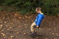 Lonely child in a blue jacket sits on a swing in a park in an autumn park, the concept of loneliness